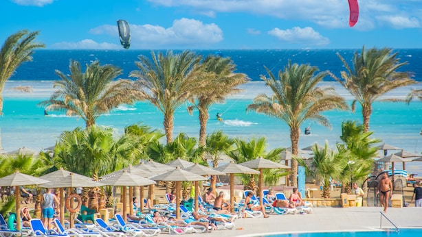 A beach resort with lounge chairs, palm trees, and a pool.