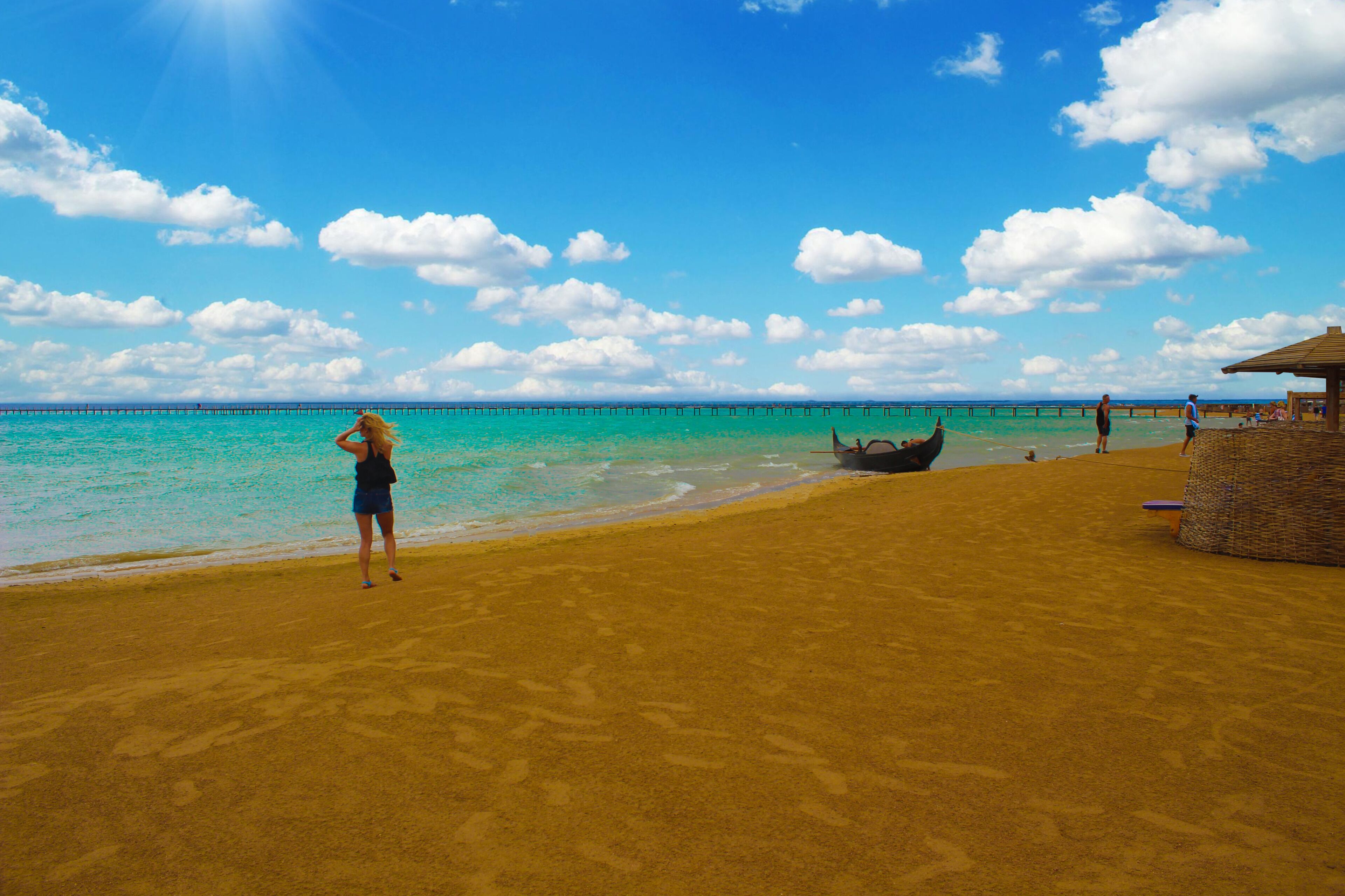 Una playa con cielo despejado, agua turquesa y una estructura de madera.