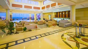A spacious lobby with multiple seating areas, a reception desk, and a view of the beach through large windows.