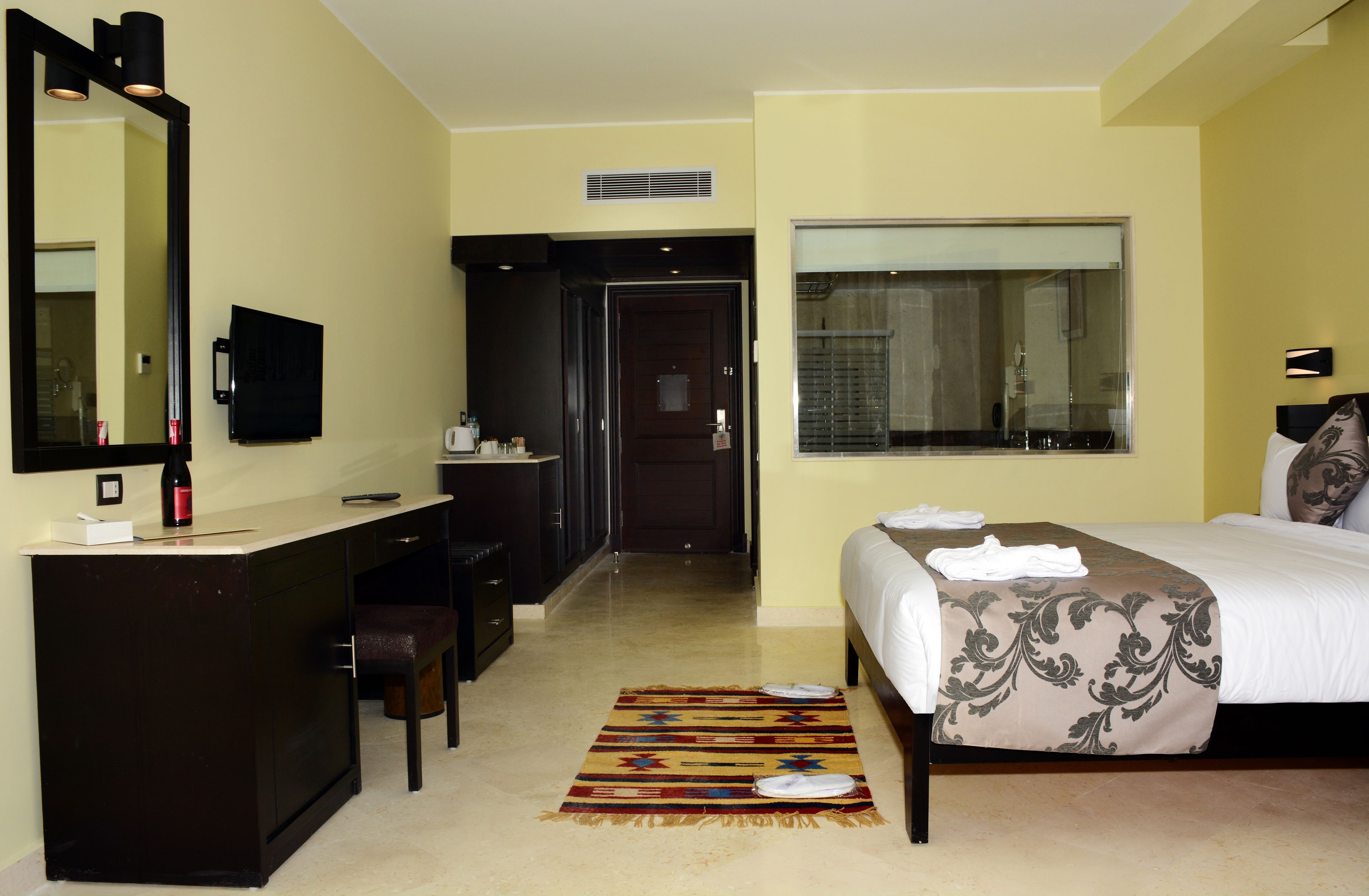 Habitación de hotel con cama, mesita de noche, espejo, escritorio, silla y ventana.