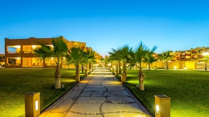 A pathway leading to a building with multiple balconies, surrounded by palm trees and well-lit by street lamps.
