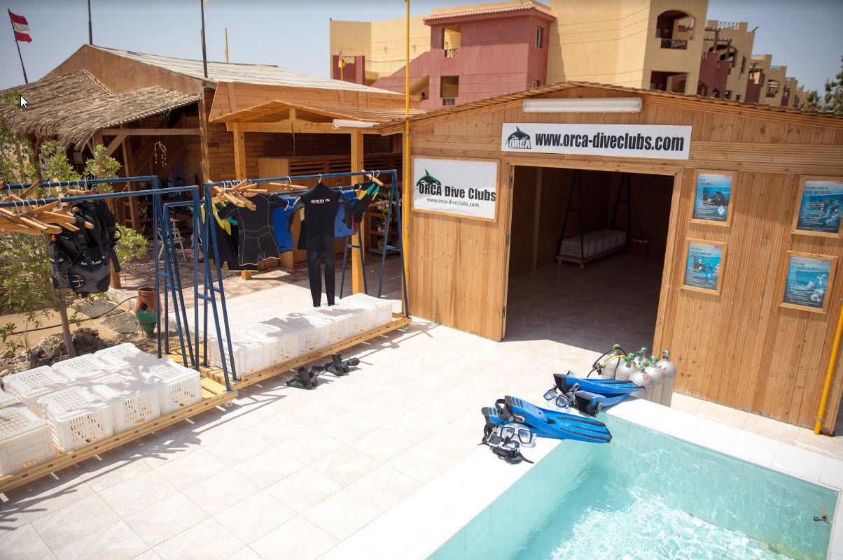 Un edificio de madera con un letrero de Orca Dive Clubs, una piscina y equipo de buceo.