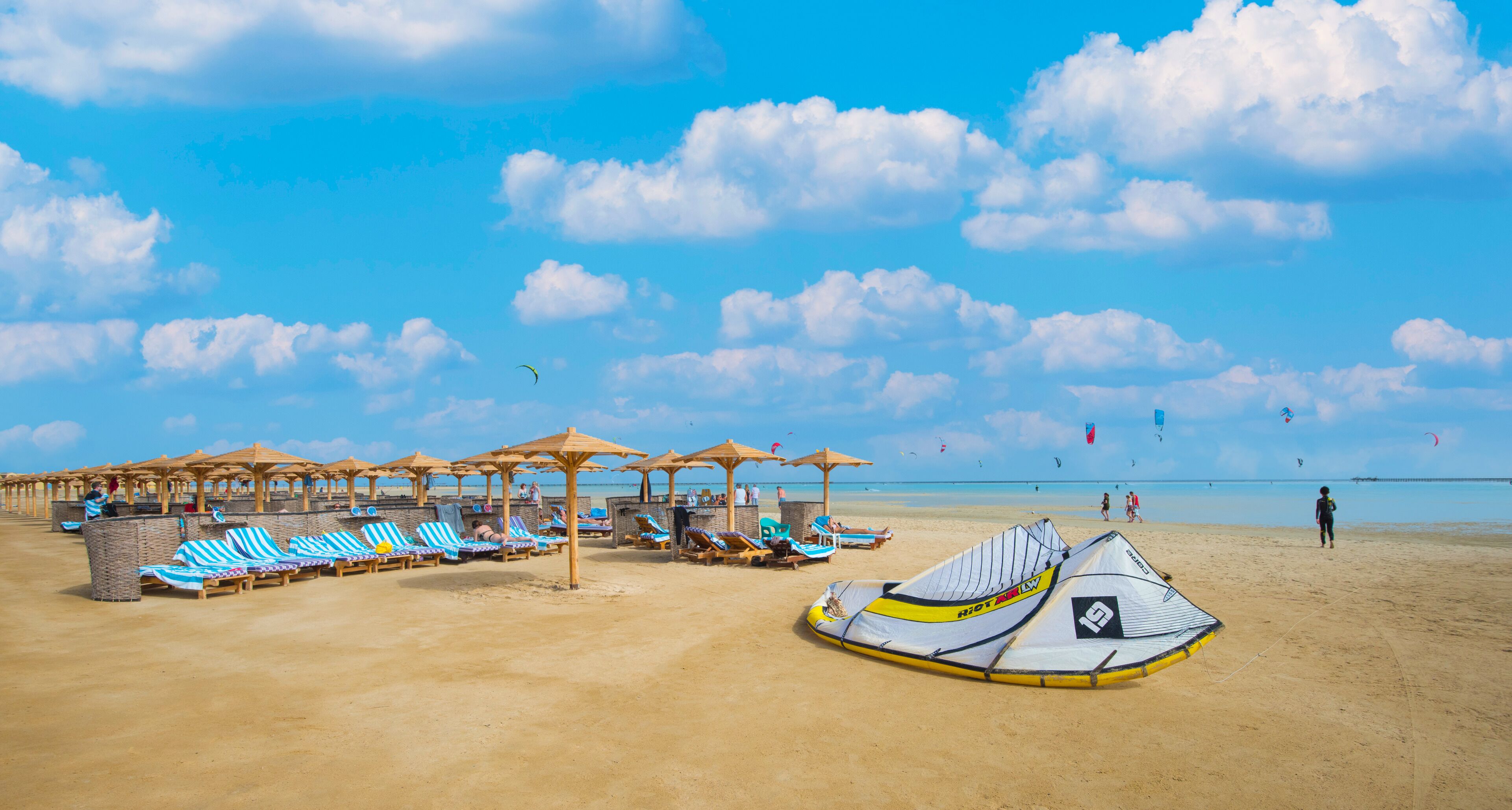 Une plage avec des transats et des parasols, un cerf-volant et un ciel dégagé.