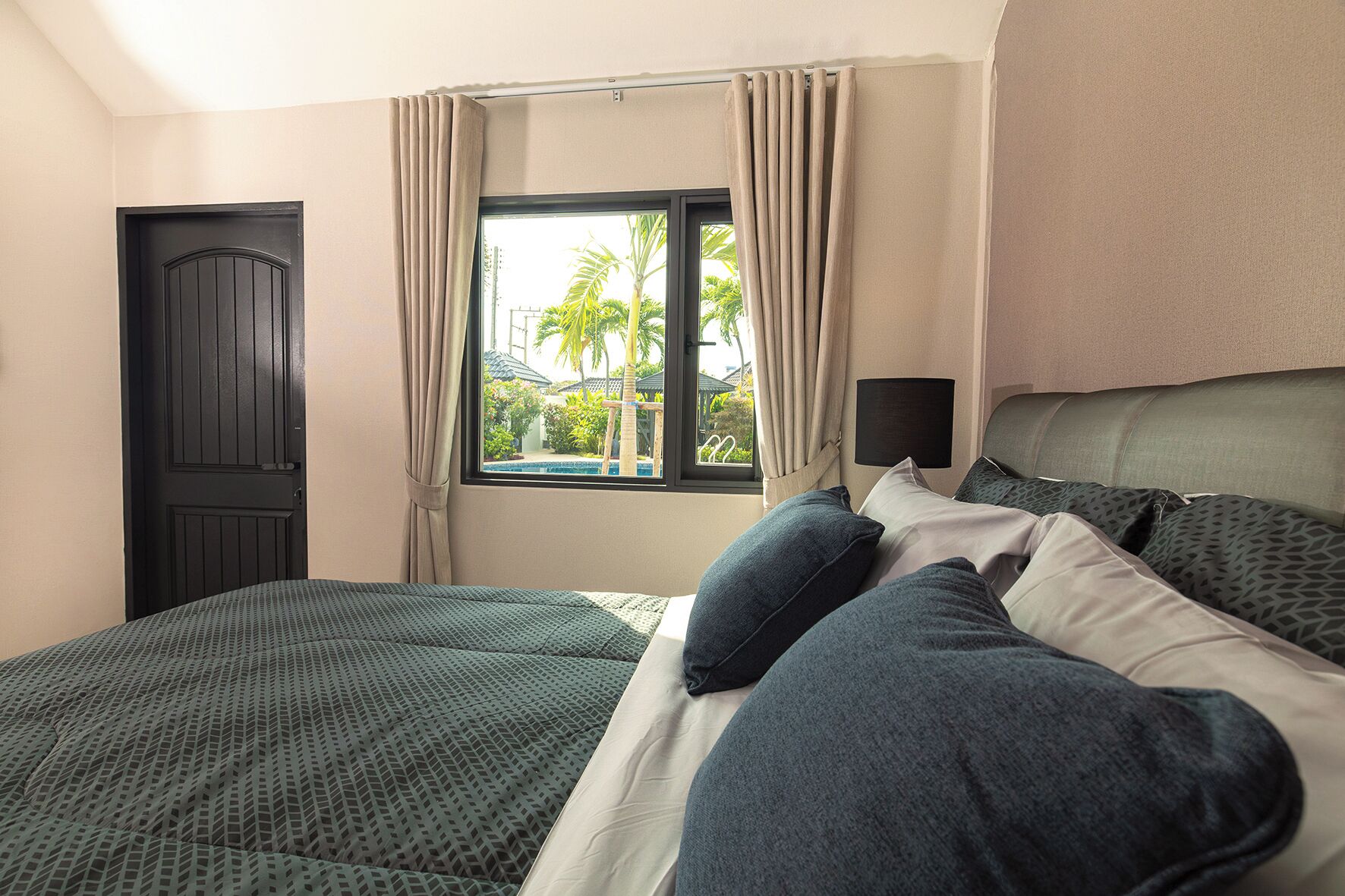 A hotel room with a bed, a window with curtains, a door, and a headboard.