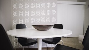 Ein runder Tisch mit einer dunklen Schüssel in der Mitte, umgeben von vier schwarzen Stühlen. An der dahinterliegenden Wand befindet sich ein weißes Blumenmuster.