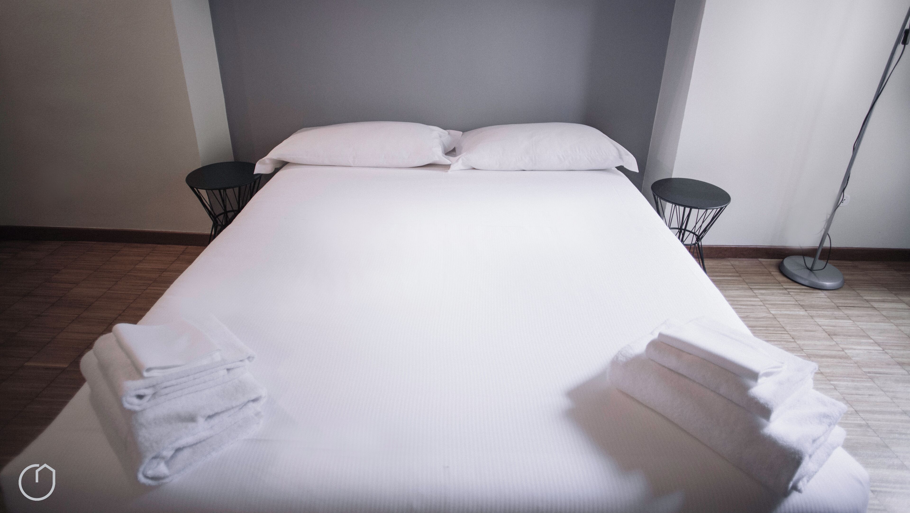 Un lit bien fait, avec des oreillers et des serviettes pliées, deux tables de chevet et une lampe sur pied dans une chambre d’hôtel.