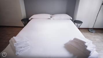 Un lit bien fait, avec des oreillers et des serviettes pliées, deux tables de chevet et une lampe sur pied dans une chambre d’hôtel.