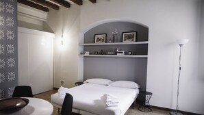 Ein Hotelzimmer mit Bett, Schreibtisch, Stuhl, Lampe und einem Regal mit Bildern und einer Vase.