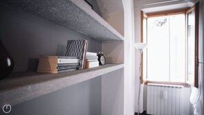 Ein Regal mit Büchern und einer Uhr, ein Heizkörper und ein Fenster mit Jalousien.