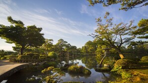 Un jardin paisible avec un étang, un pont de pierre et une pagode japonaise traditionnelle.