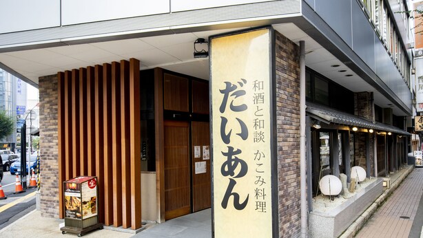 Un restaurant avec une grande enseigne en japonais, une façade en briques et un trottoir orné d’une affiche.