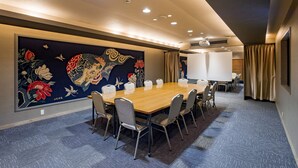 Une salle de conférence avec une longue table, des chaises, une grande tapisserie et un tableau blanc.
