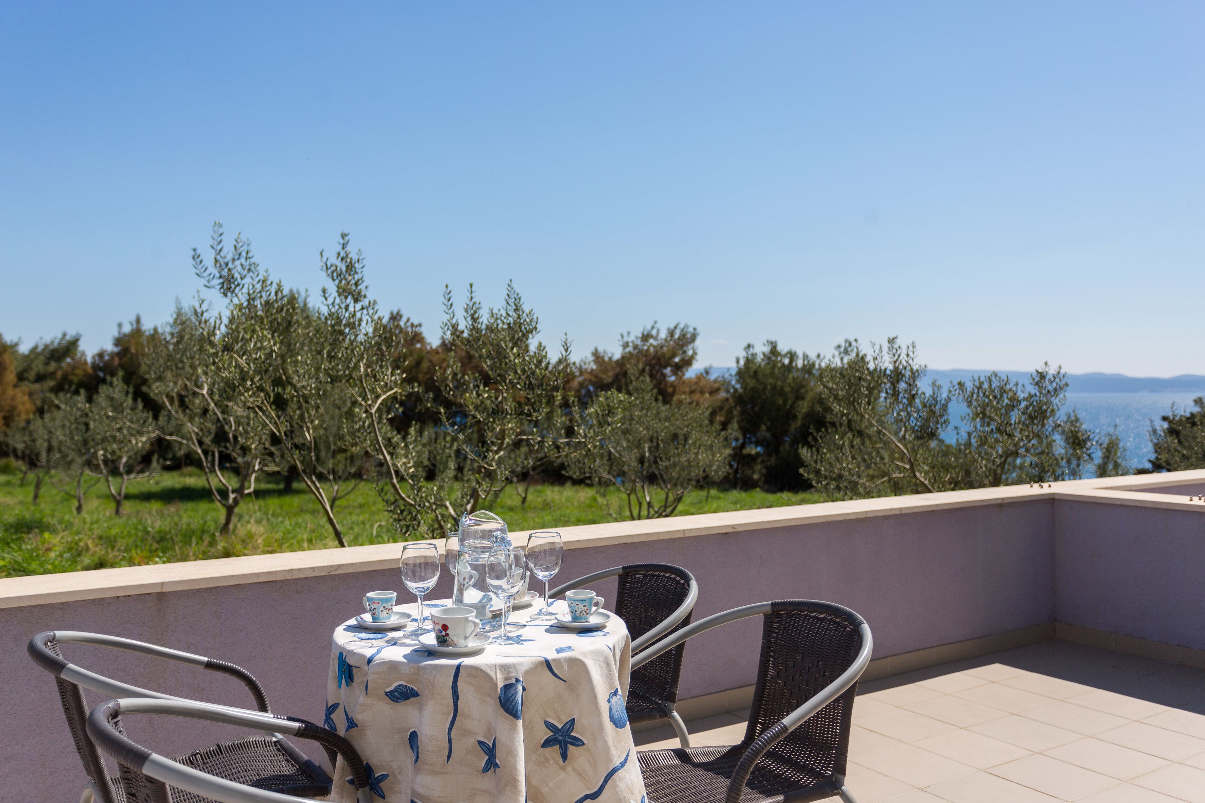A round table with a floral tablecloth, surrounded by metal chairs, overlooking a scenic view of trees and water.