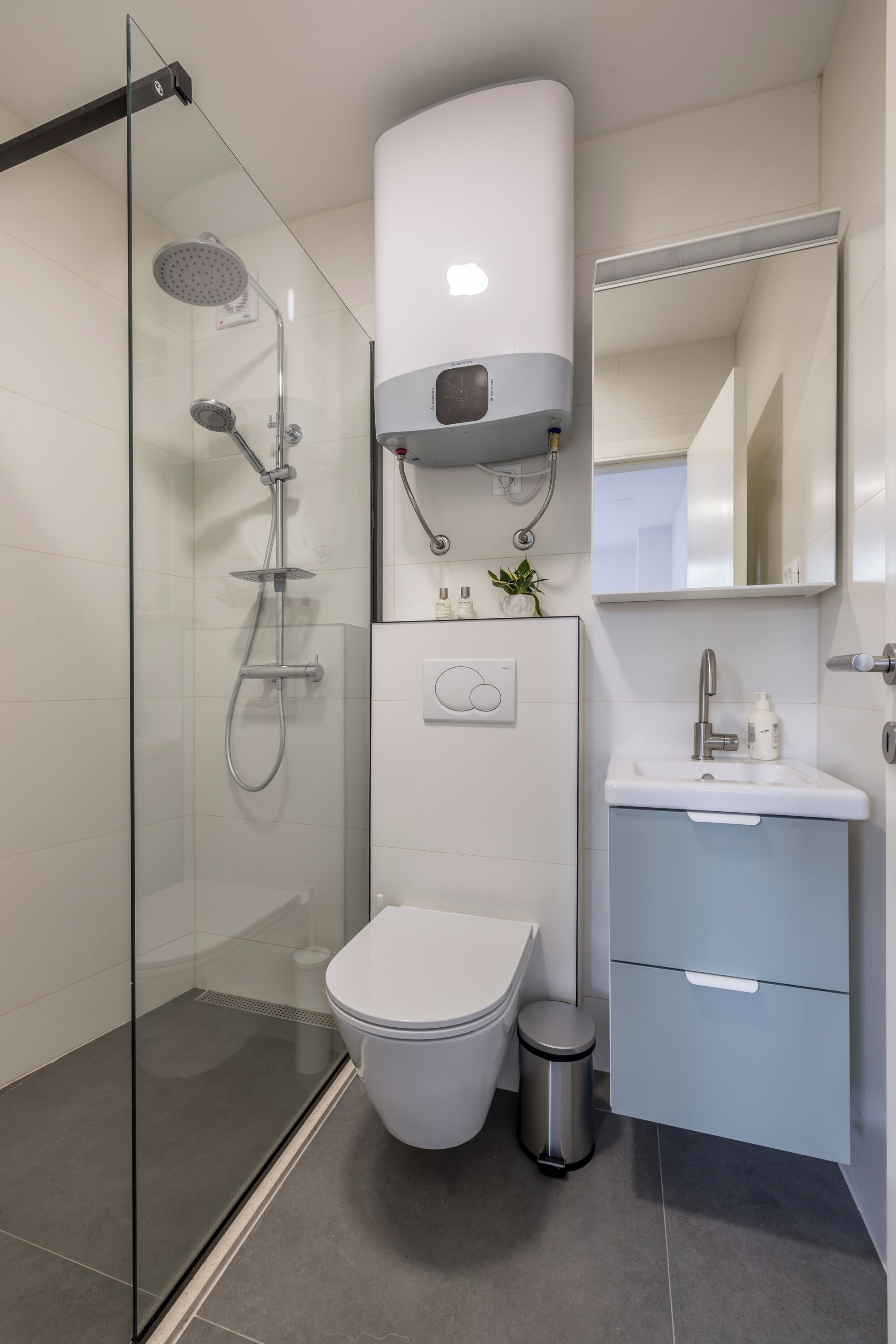 A modern bathroom with a glass-enclosed shower, a toilet, a sink with a mirror, and a compact storage unit.
