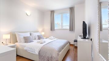 A modern hotel room with a neatly made bed, a television, and a large window with curtains.