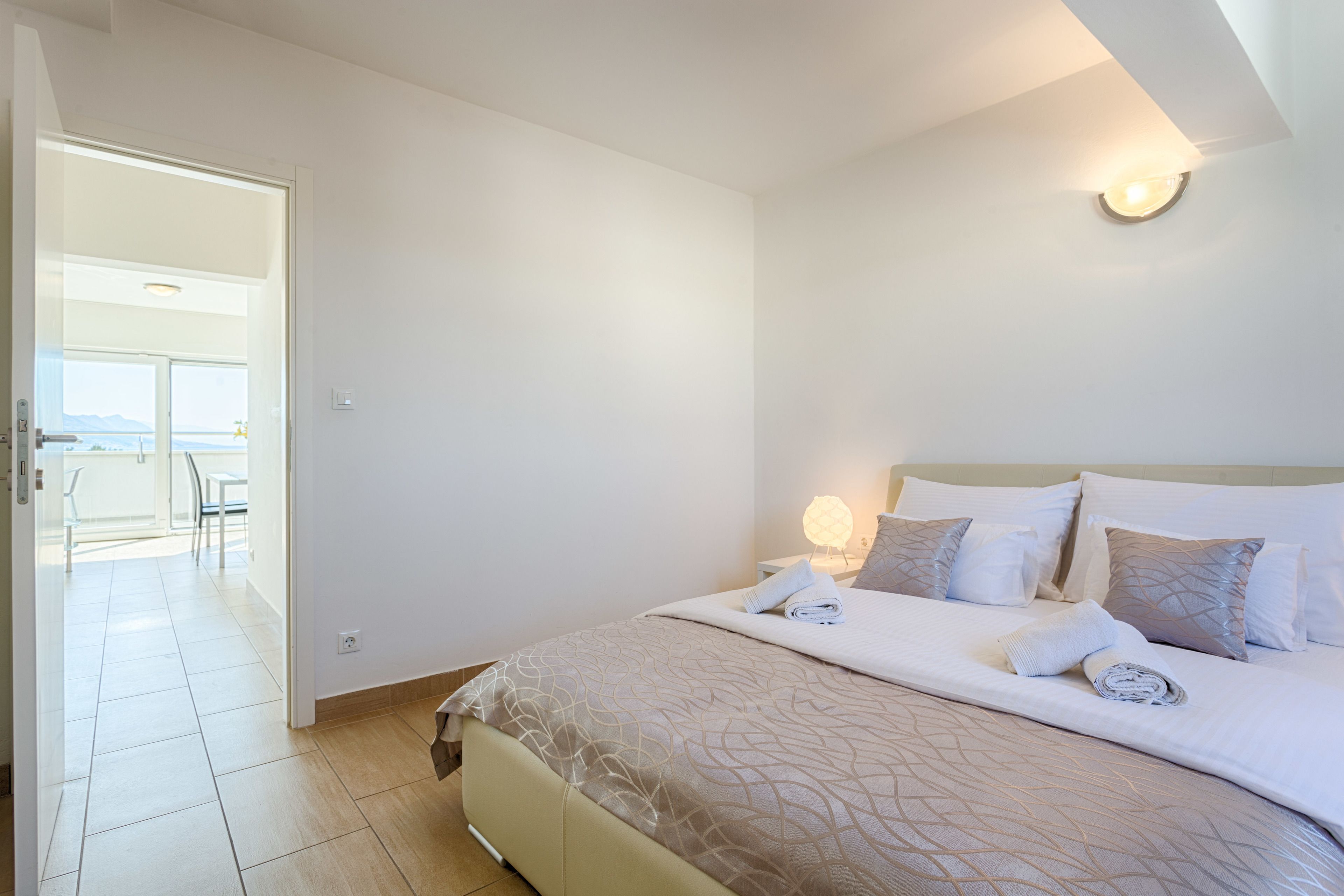Een hotelkamer met een bed, nachtkastje, lamp en uitzicht op het balkon.