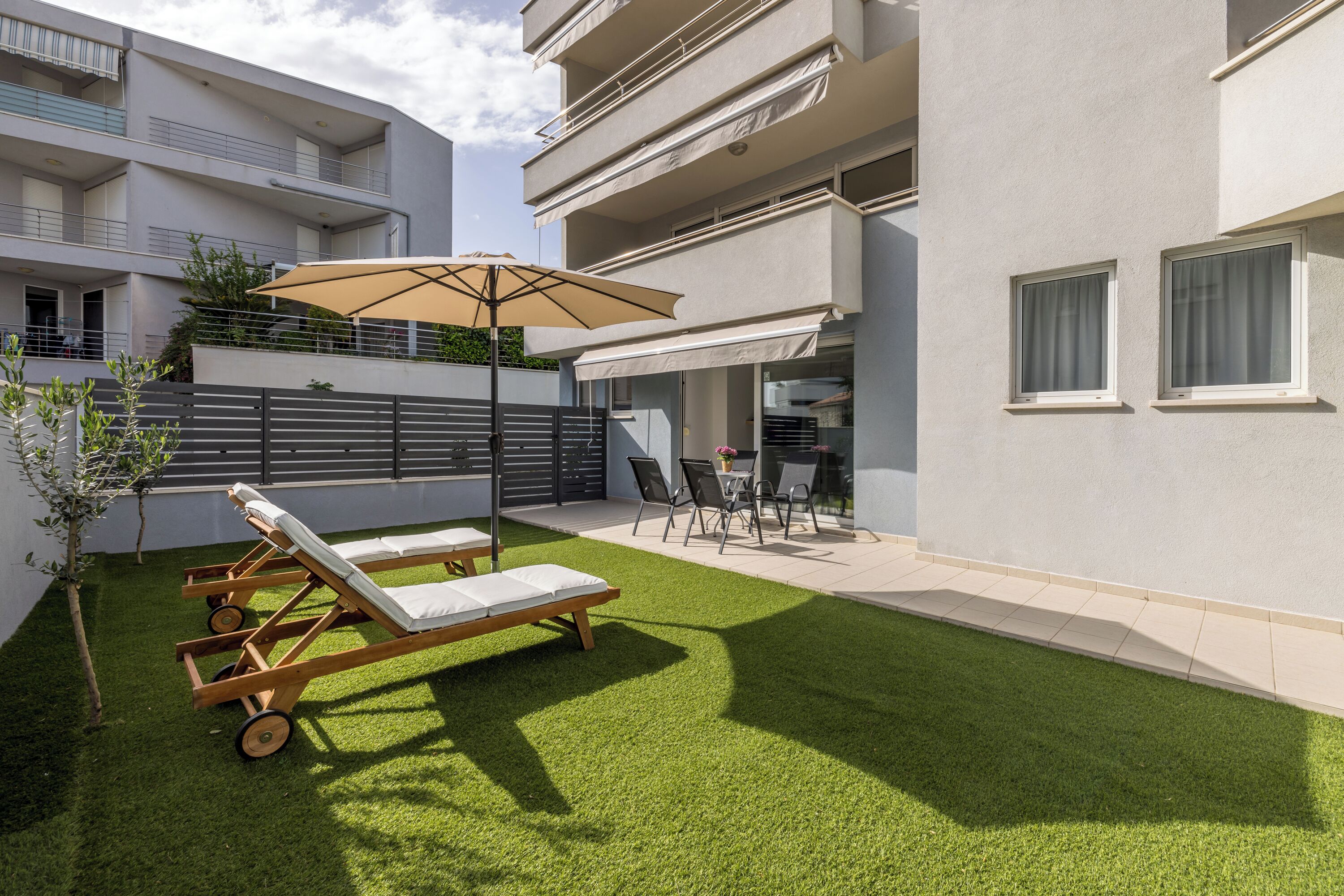 A modern apartment with a small balcony, a wooden lounge chair, and a table with chairs.
