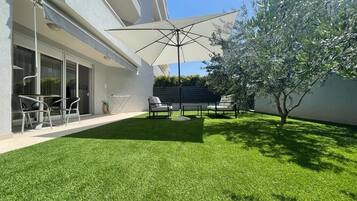 A modern outdoor patio with a well-maintained lawn, outdoor furniture, and a large umbrella providing shade.
