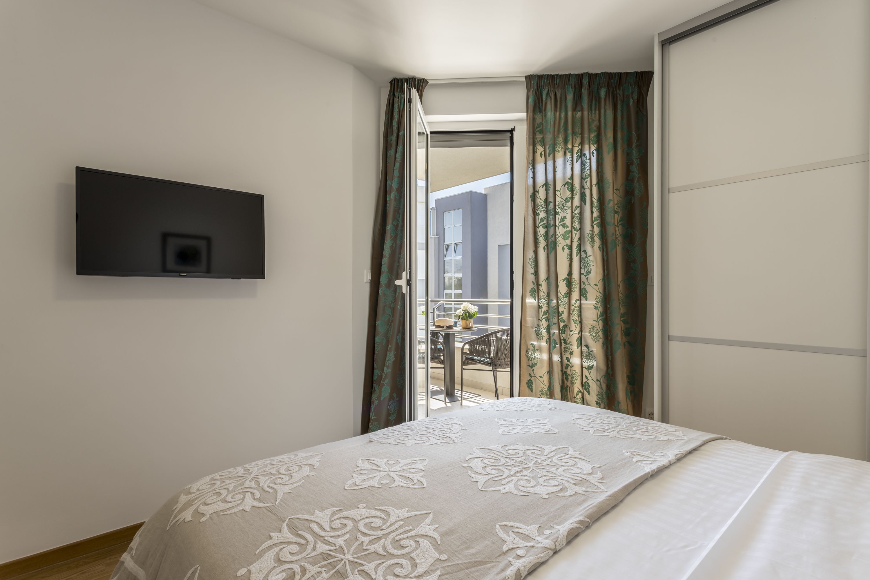 Een slaapkamer met een bed, een aan de muur bevestigde televisie en een schuifdeur naar een buitenruimte.