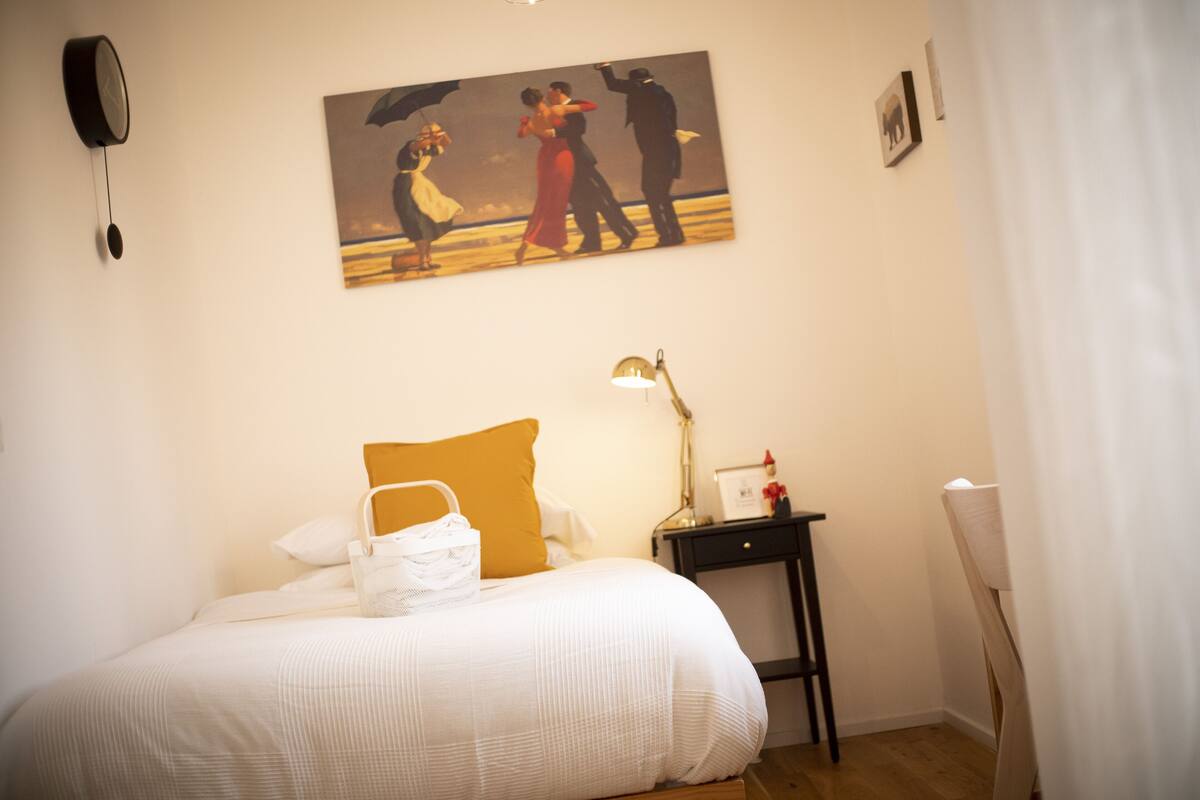 Un dormitorio con una cama, una mesita de noche, una lámpara, un cuadro y un reloj en la pared.