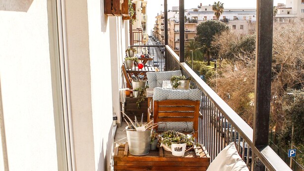 Un balcon agrémenté de meubles en bois, de plantes en pot et offrant une vue sur le paysage urbain.
