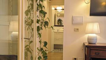 Ein Flur mit Holzboden, einer Pflanze, einer roten Bank, einem an der Wand befestigten Fernseher und einer Lampe.