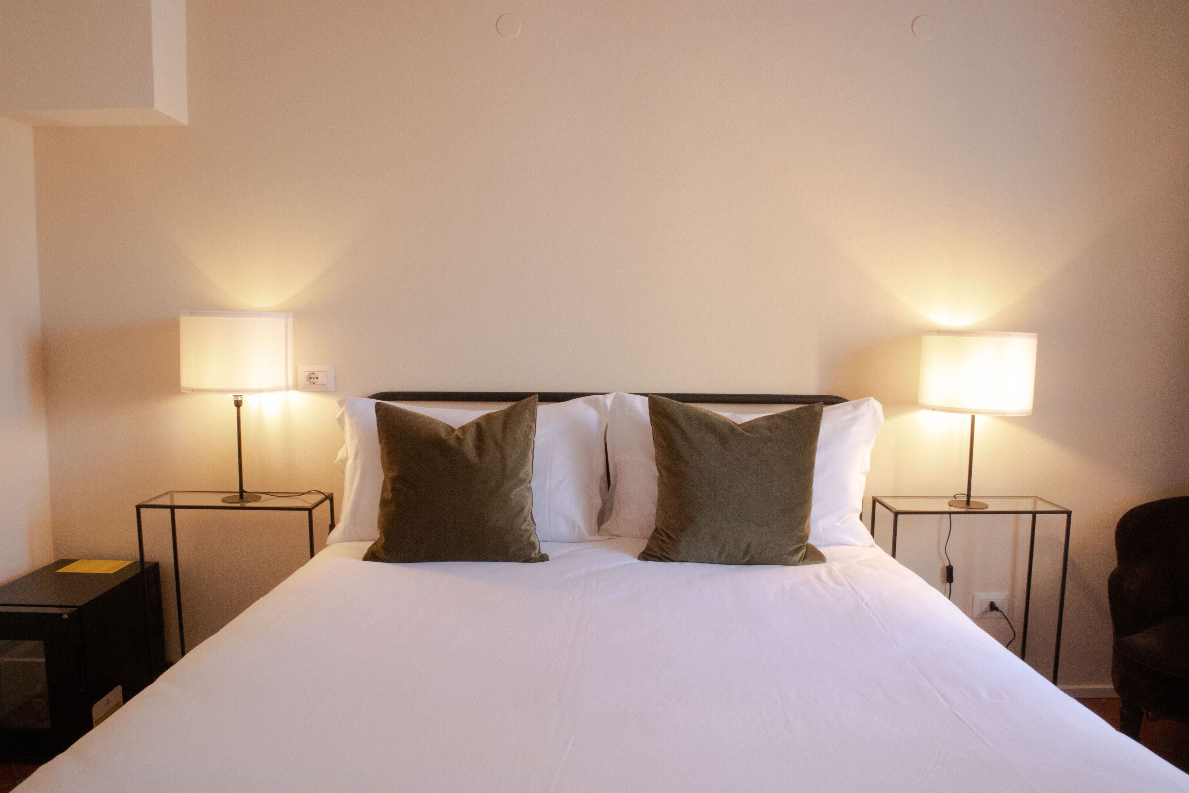 Una habitación de hotel con una cama grande, dos lámparas de noche y una silla.