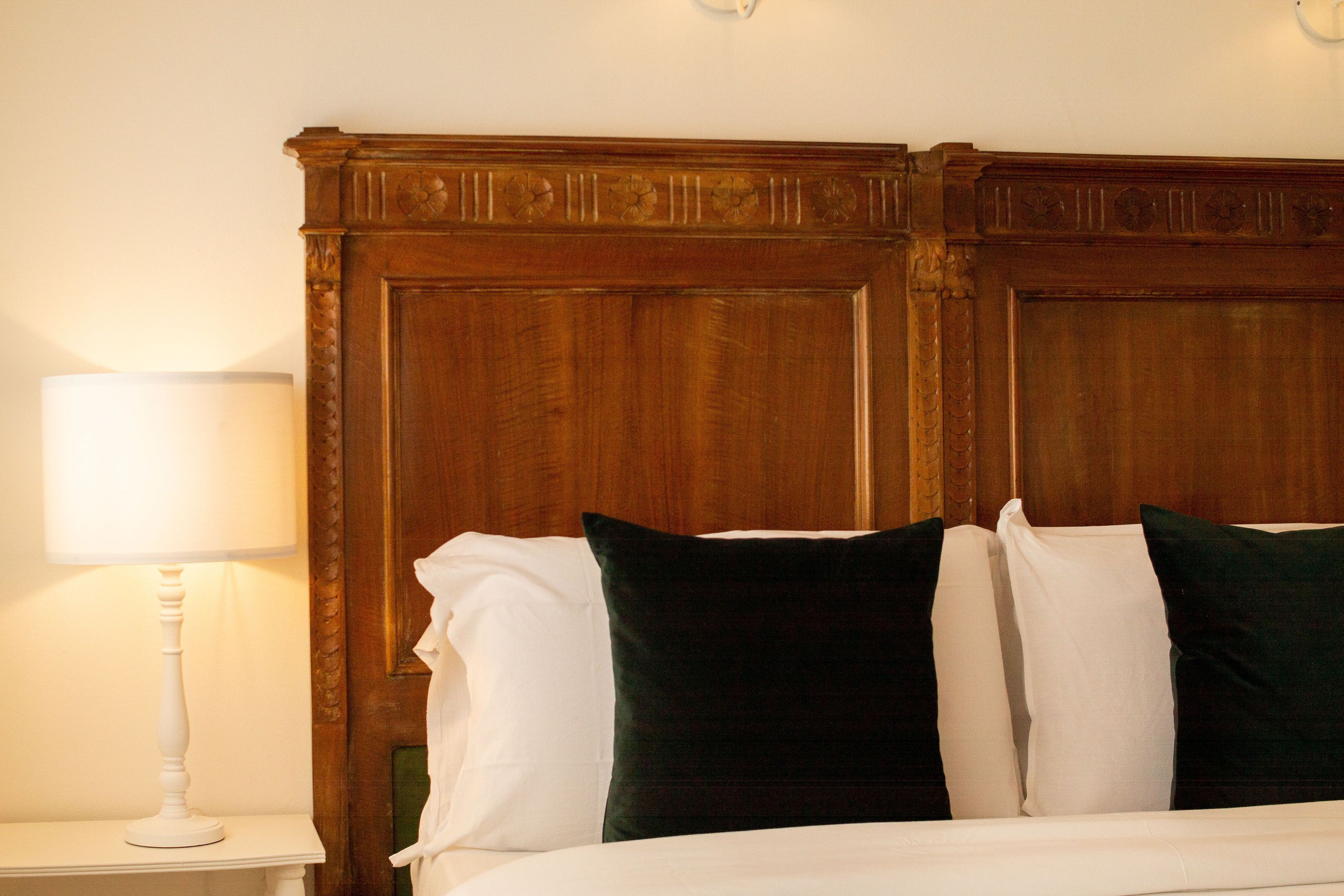 Una cama bien hecha con almohadas blancas y verdes, un cabecero de madera y una lámpara de noche blanca.