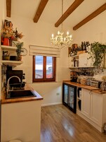 Cucina con travi in legno, un lampadario, una finestra con vista e scaffali pieni di bottiglie.
