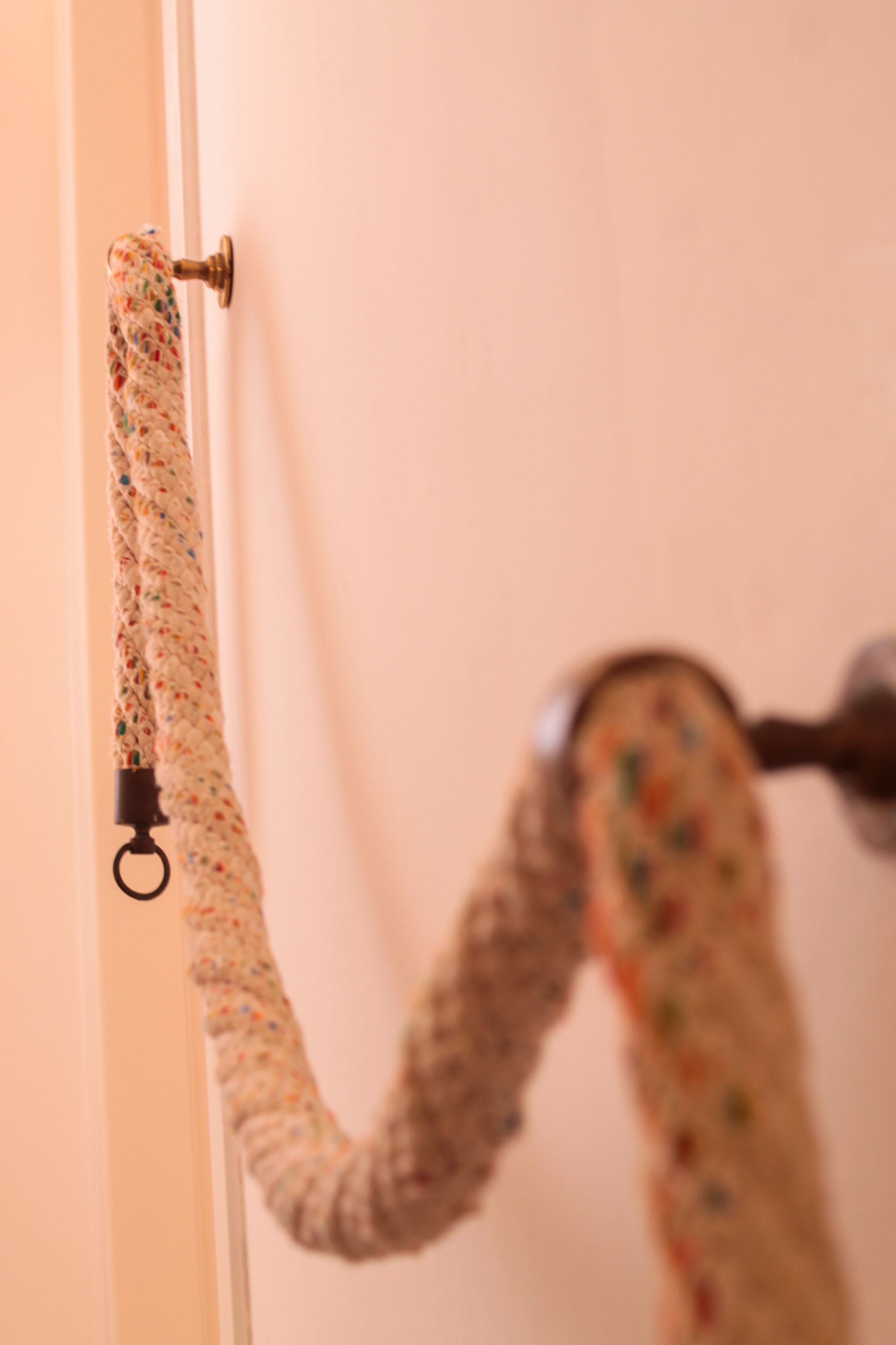 A door with a braided, multicolored rope hanging on a metal hook.