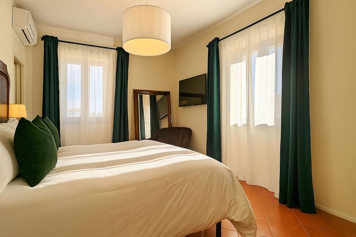 A hotel room with a large bed, a chair, a TV, and curtains.