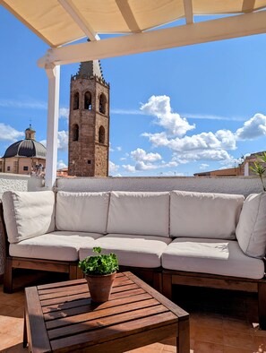 A covered outdoor seating area with a wooden table and a potted plant, overlooking a historic tower and dome structure. - Panorama Guest House (Alghero)