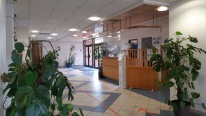 A reception area with a counter, potted plants, and a tiled floor with directional arrows. - Hotel Villenouvelle (Montauban)