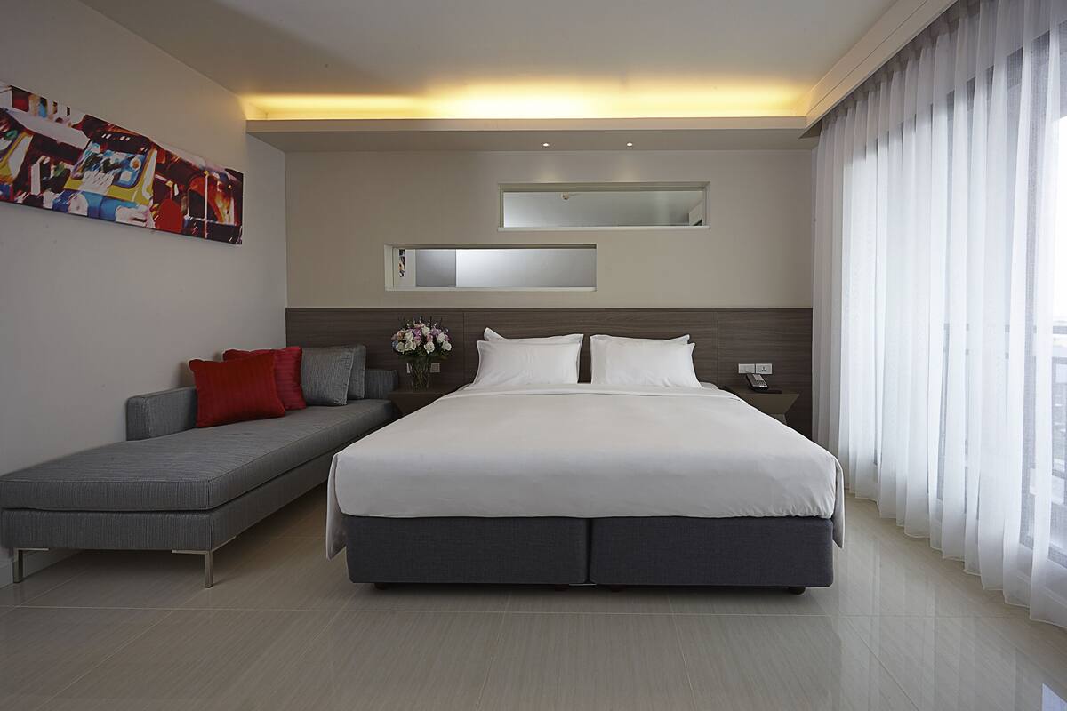A modern bedroom with a large bed, a sofa, a nightstand, and a mirror.