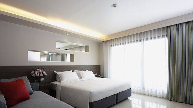 Una habitación de hotel moderna con una cama grande, un sofá, un espejo y una ventana con cortinas.