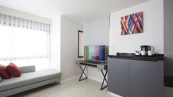 A modern living room with a grey sofa, a flat-screen TV, a coffee maker, and a colorful abstract painting on the wall.