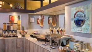 Een buffetgedeelte met diverse keuzes, waaronder een fruitschaal, een buffetstation en een schilderij aan de muur.