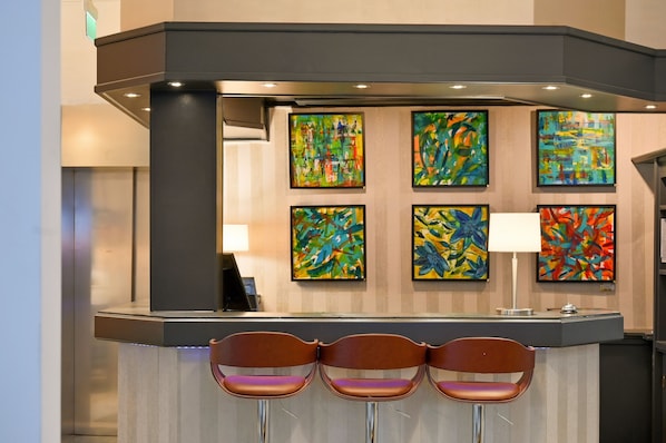 A reception area with a counter, three brown chairs, and six colorful abstract paintings on the wall.