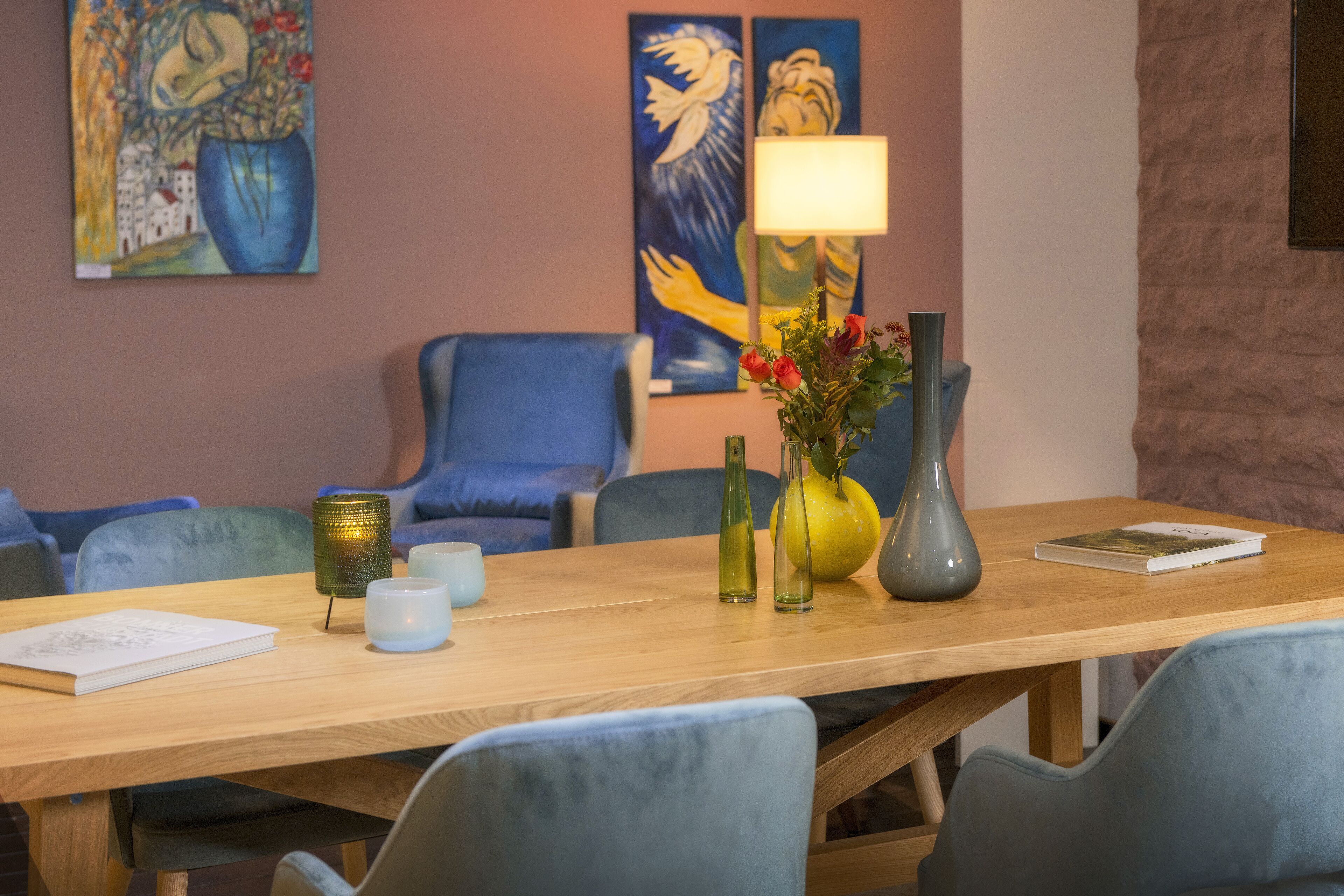 A wooden table with a book, candles, and vases. There are blue chairs around the table.