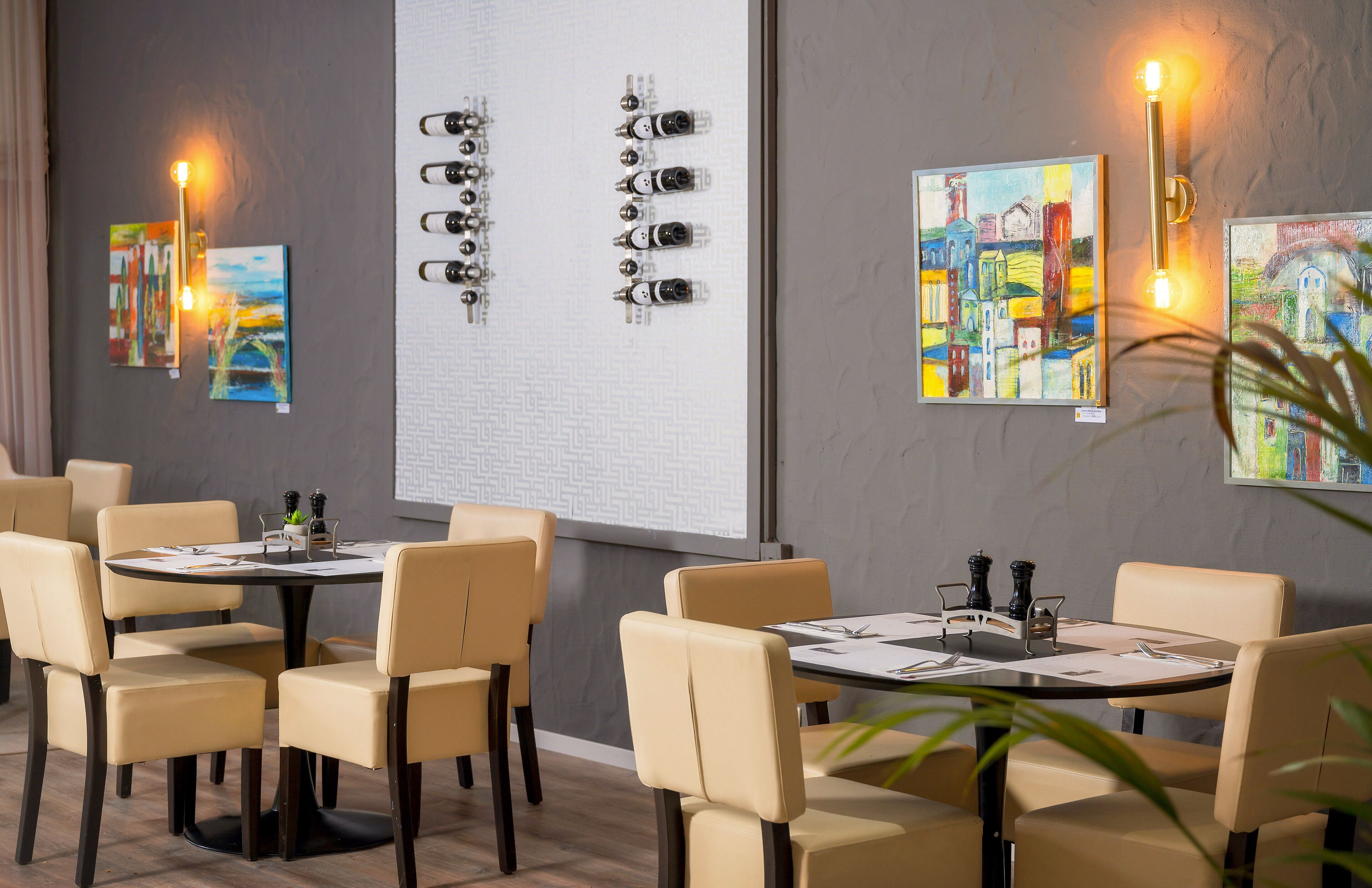 A dining area with round tables, beige chairs, and wall-mounted light fixtures.