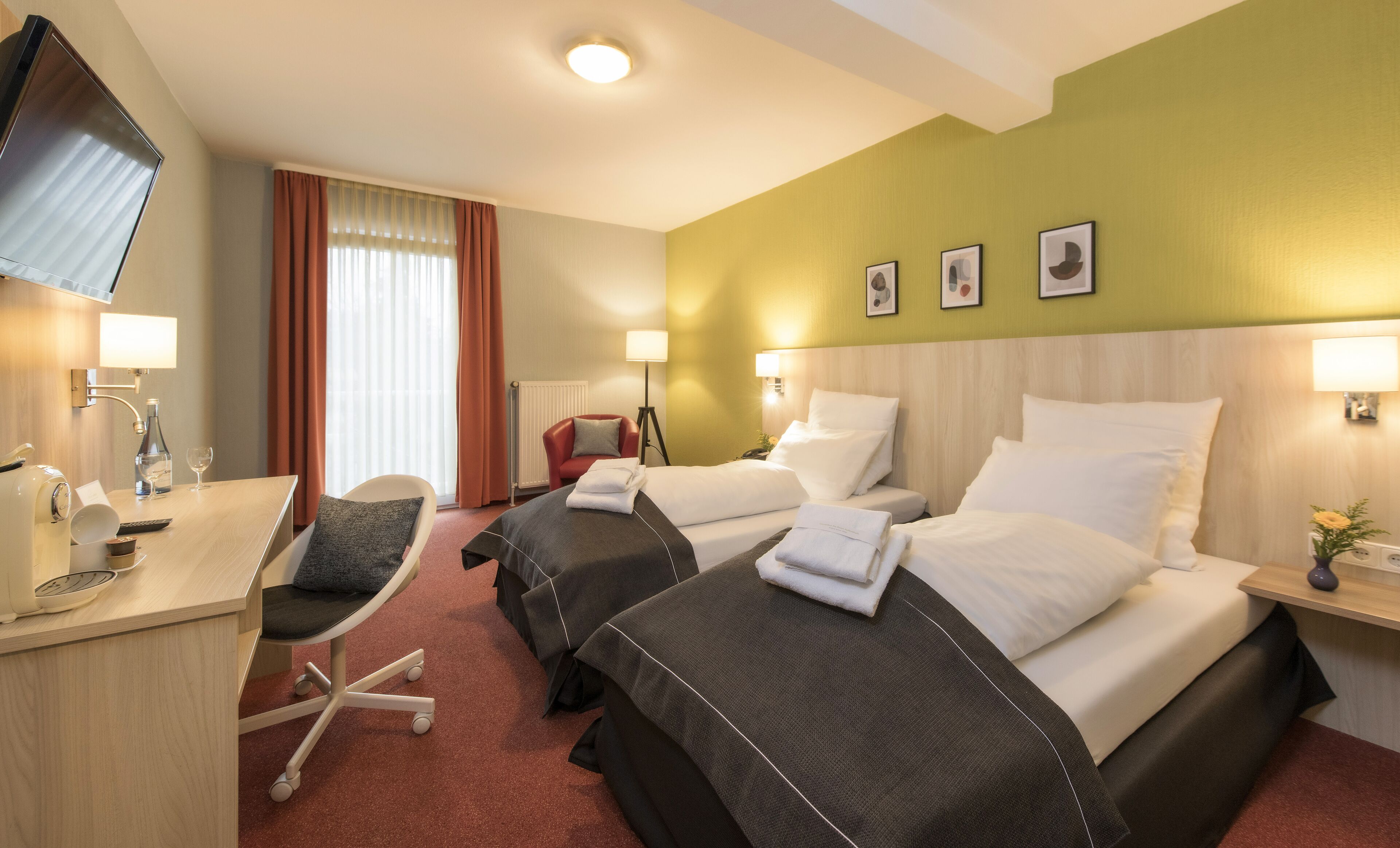 Hotellihuone, jossa on kaksi sänkyä, työpöytä tuolilla, televisio ja ikkuna, jossa on verhot.