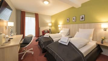 Hotellihuone, jossa on kaksi sänkyä, työpöytä tuolilla, televisio ja ikkuna, jossa on verhot.