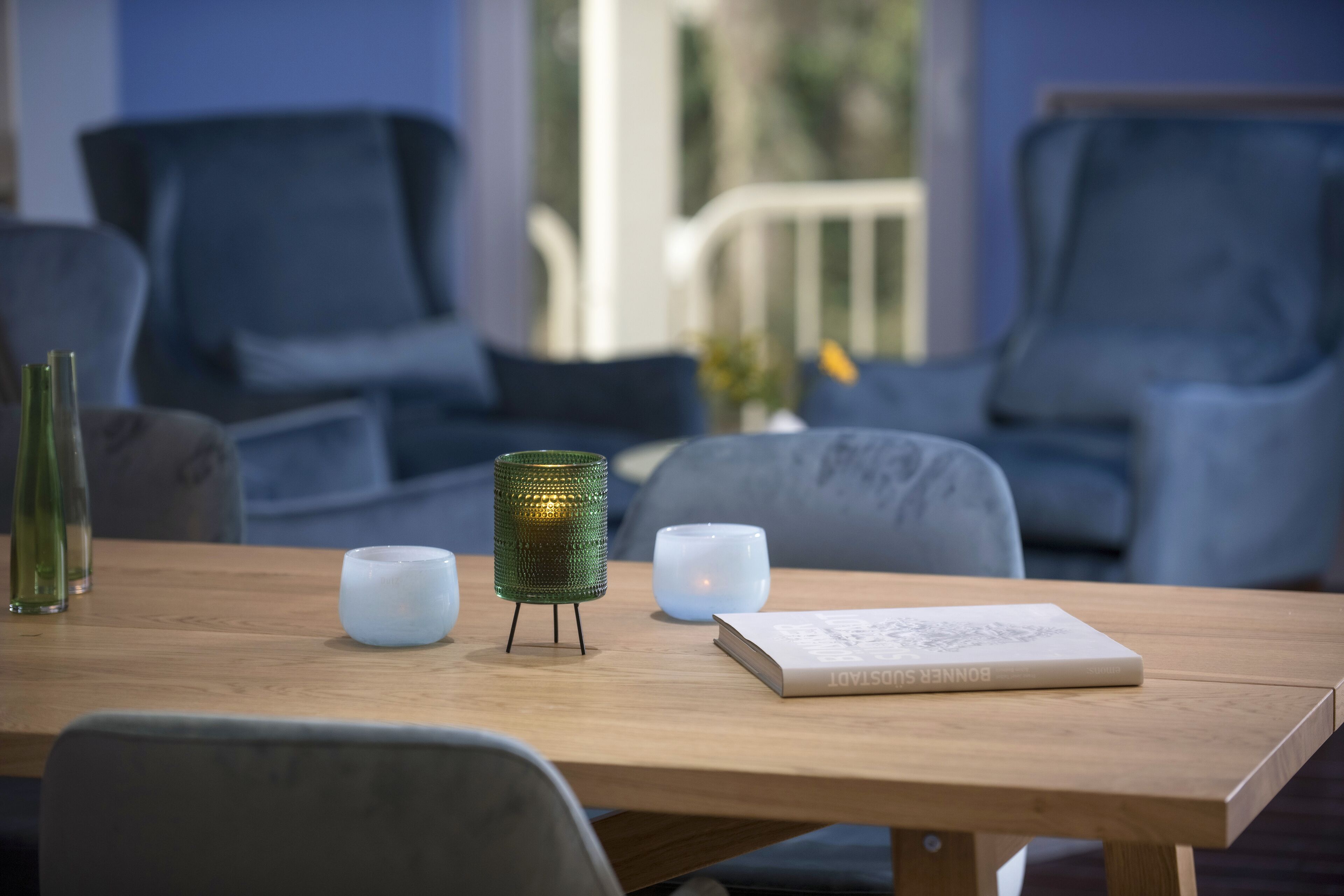 A wooden table with three candles, a book, and a green candle holder.