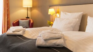 Habitación de hotel con una cama bien hecha, dos almohadas, una silla roja y una lámpara.