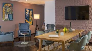 A modern conference room with a wooden table, blue chairs, a standing lamp, and artwork on the walls.
