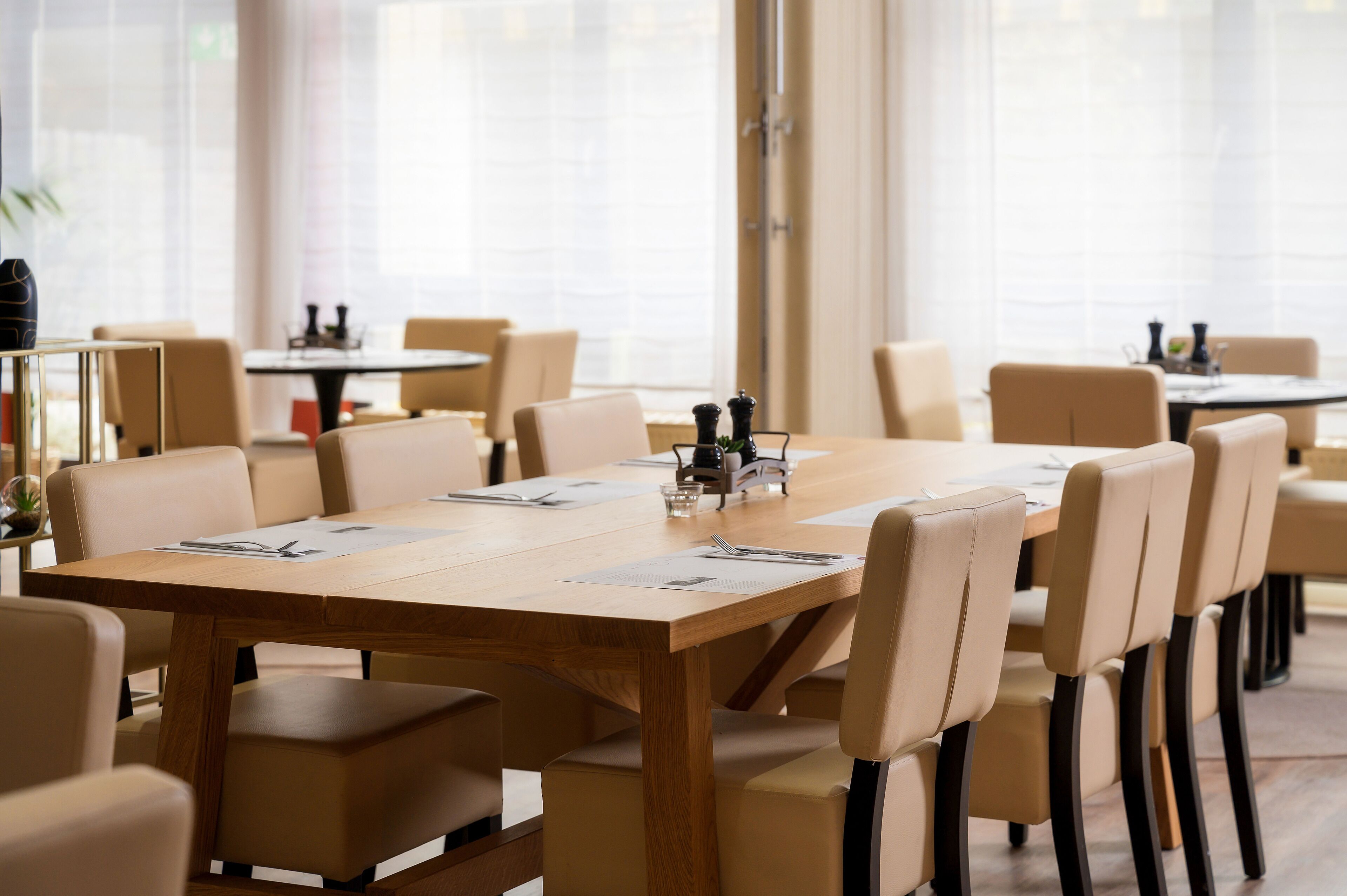 Un salón de conferencias con una larga mesa, sillas color beige y una mesa pequeña con aderezos.