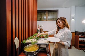 A buffet setup with various food items and a person serving. - Maesa Hotel (Ponorogo)