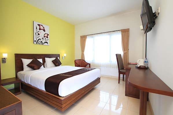 Una habitación de hotel con una cama grande, un escritorio, una silla, un televisor montado en la pared y una ventana con cortinas.