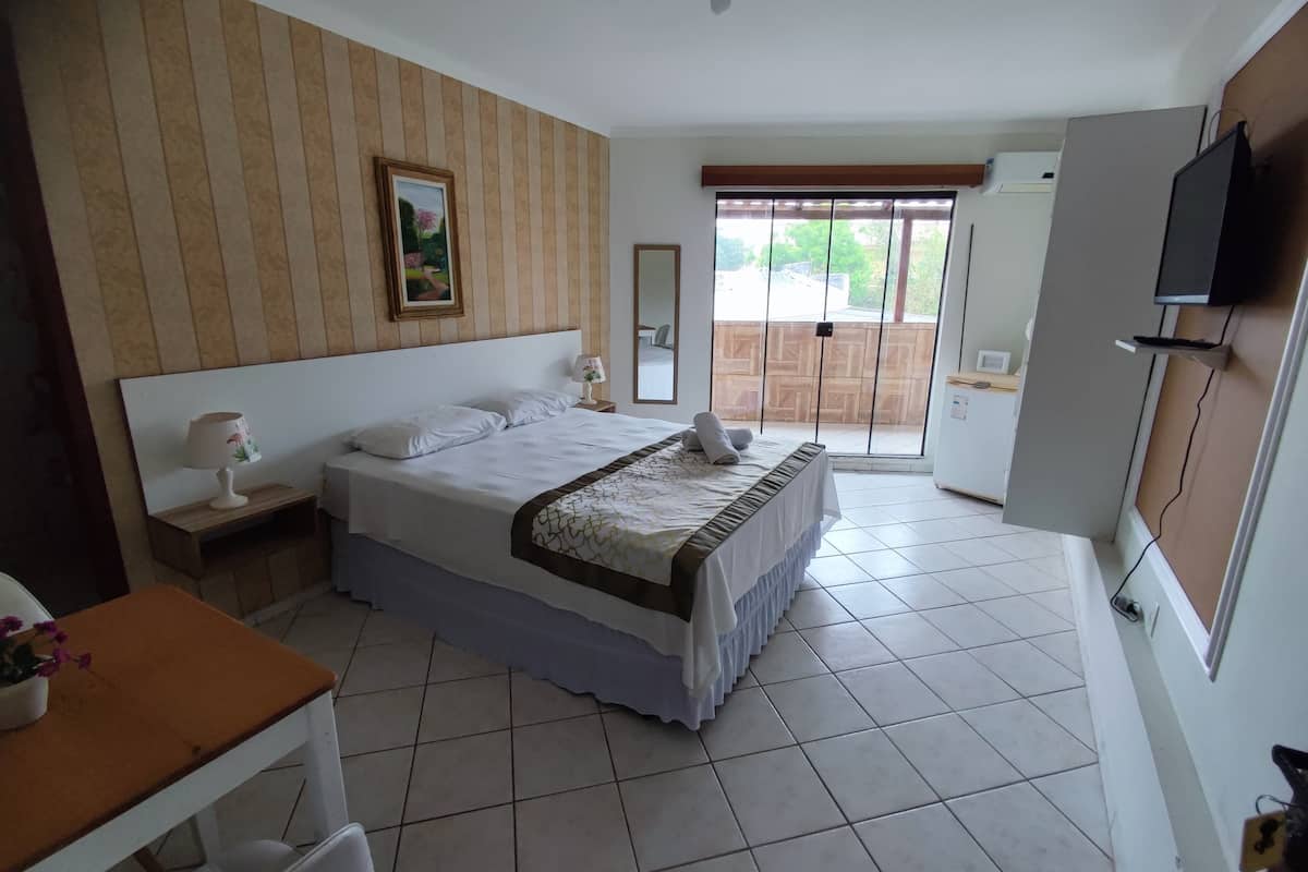 Quarto de hotel com uma cama grande, escrivaninha, cadeira, televisão e vista para o exterior.