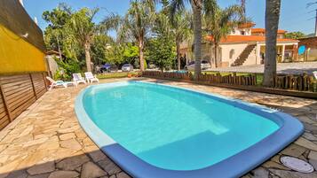 Piscina con baldosas de piedra, rodeada de palmeras y sillas de descanso.